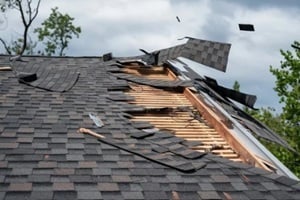 roof severely damaged by strong winds, with missing shingles and exposed wooden beams